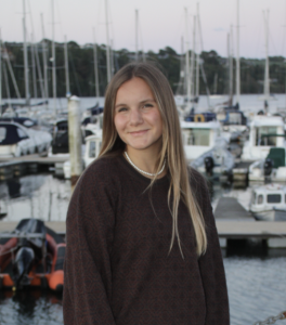 A woman smiles with boats behind her. 